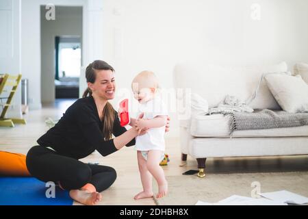 Allegra madre lavoratrice che tiene figlia mentre si esercita in soggiorno in ufficio a casa Foto Stock