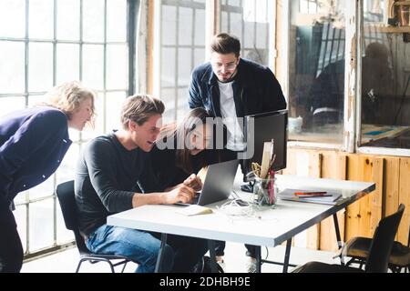 Curiosi colleghi che guardano al programmatore di computer maschile che codifica nel laptop sul posto di lavoro Foto Stock