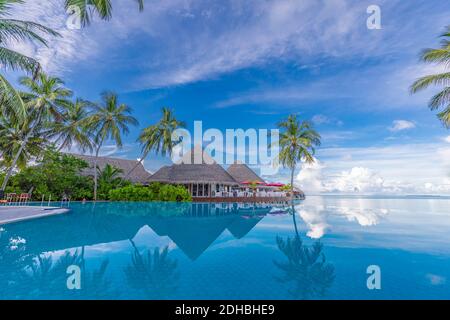 Paesaggio turistico estivo di lusso. Lussuoso resort sulla spiaggia, piscina a riflessione e sedie a sdraio, ombrelloni palme cielo blu a bordo piscina Foto Stock