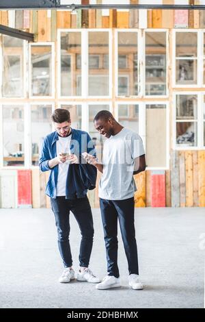 Tutta la lunghezza dei messaggi di testo sorridenti degli uomini d'affari utilizzando i telefoni cellulari sul luogo di lavoro creativo Foto Stock