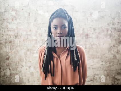 Ritratto di programmatore femminile sicuro con dreadlock in piedi contro la parete in ufficio Foto Stock
