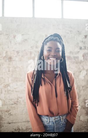 Ritratto di giovane donna esperto IT sorridente mentre si sta in piedi contro parete in ufficio Foto Stock