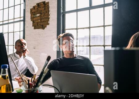 Professionisti IT di sesso maschile sicuri che guardano lontano mentre si siedono a bordo sala durante la riunione Foto Stock