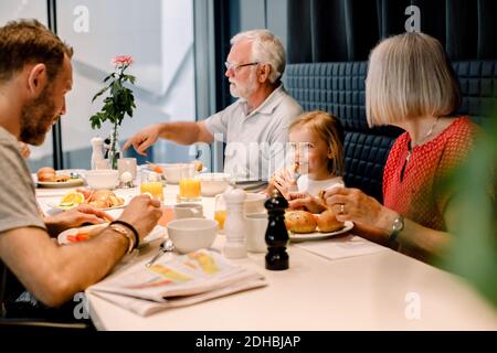 Sorridente ragazza che guarda il padre mentre si mangia con i nonni al ristorante Foto Stock