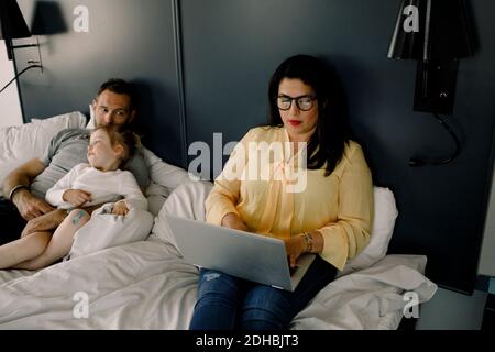 Vista ad alto angolo di una donna che utilizza il computer portatile mentre si è seduti uomo e figlia a letto Foto Stock