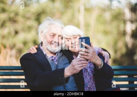 Sorridente coppia senior che prende selfie mentre si siede sulla panchina Foto Stock