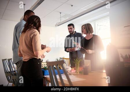 Ingegneri maschili e femminili in piedi al tavolo mentre lavorano insieme su progetto in ufficio Foto Stock