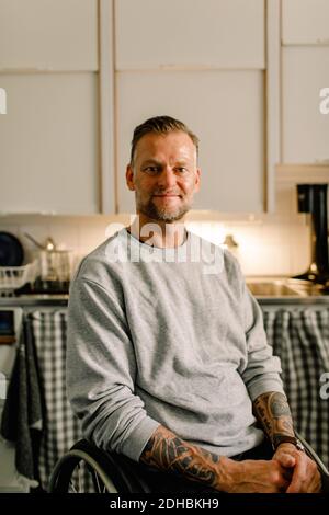 Ritratto di un uomo inabile sorridente e sicuro seduto su una sedia a rotelle cucina a casa Foto Stock