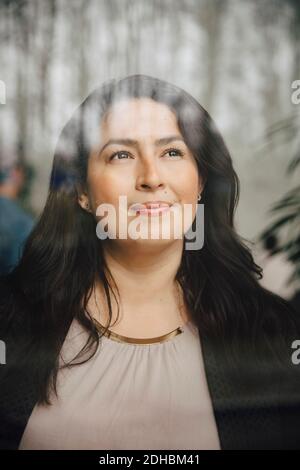 Pensieroso imprenditore femminile che guarda attraverso la finestra mentre in piedi in ufficio Foto Stock