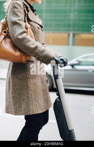 Vista laterale sezione centrale di businesswoman che guida scooter elettrico a spinta dentro città Foto Stock