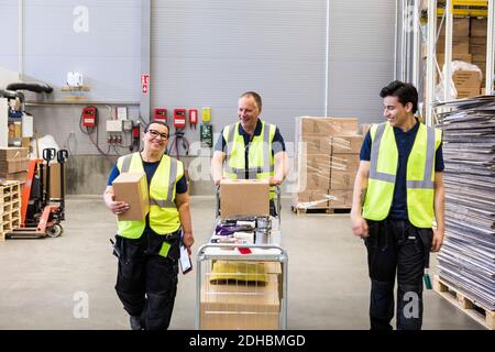 Sorridenti colleghi multietnici che camminano con il carrello al magazzino di distribuzione Foto Stock