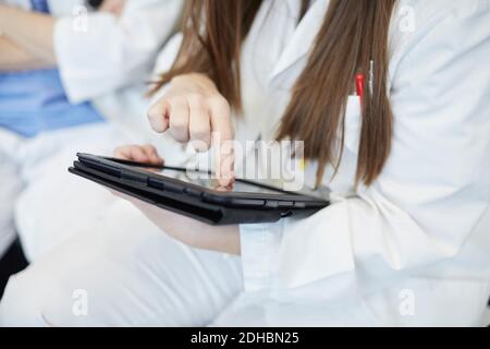 Sezione centrale della giovane dottoressa che usa la tavoletta digitale mentre si è seduti in corridoio all'ospedale Foto Stock