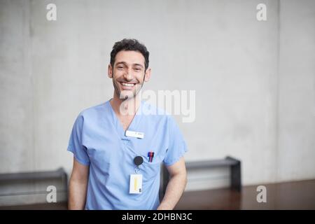 Ritratto di giovane infermiera sorridente in scrub blu in piedi contro il muro all'ospedale Foto Stock