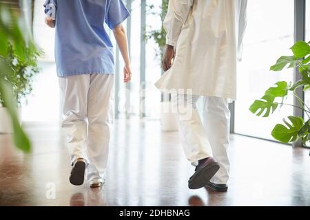 Bassa sezione dell'infermiera femminile che cammina con il medico maschio dentro corridoio all'ospedale Foto Stock