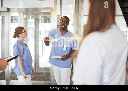 Un'infermiera maschile sicura che dà documento al medico nella lobby all'indirizzo ospedale Foto Stock