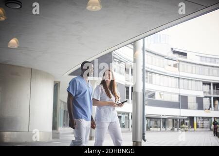 Infermieri fiduciosi discutere mentre camminando sul sentiero all'ospedale visto attraverso il vetro Foto Stock