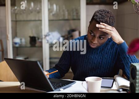 Ragazzo preoccupato che guardava il computer portatile mentre faceva i compiti tabella Foto Stock