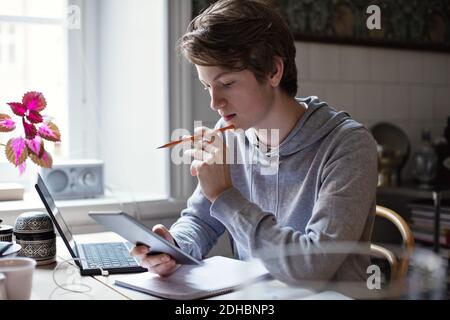 Un adolescente serio che usa un tablet digitale mentre fa i compiti tabella Foto Stock