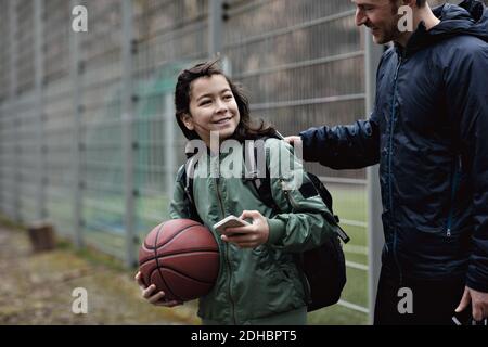 Sorridente figlio che guarda il padre mentre si trova sul campo da gioco Foto Stock
