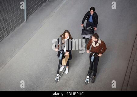 Vista ad alto angolo degli amici adolescenti che cavalcano gli scooter elettrici a spinta e in bicicletta sulla strada in città Foto Stock