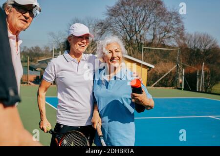 Amici anziani felici che guardano via mentre tengono la racchetta di tennis a. campo Foto Stock