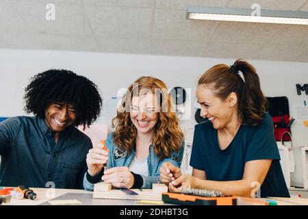 Sorridenti tecnici multietnici che lavorano sul legno al banco di lavoro in creativo ufficio Foto Stock