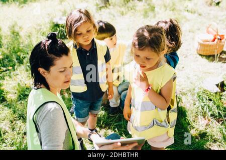 Visualizzazione ad alto angolo di una insegnante di sesso femminile che condivide un tablet digitale con studenti nel parco giochi Foto Stock