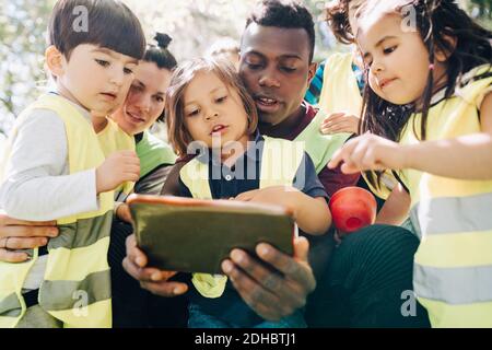 Studenti e insegnanti multietnici che condividono un tablet digitale nel parco giochi Foto Stock