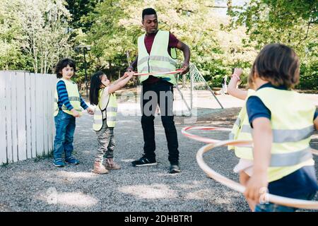 Insegnante di sesso maschile e studenti che giocano con cerchi di plastica nel parco giochi Foto Stock