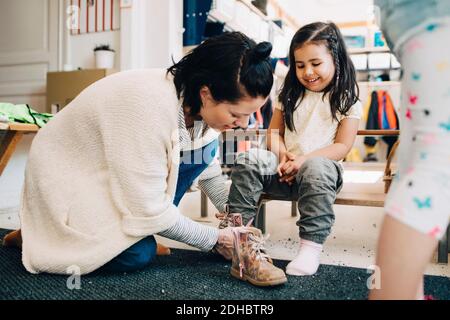 Vista laterale dell'insegnante che aiuta la ragazza felice che indossa le scarpe dentro guardaroba presso lo sgabello Foto Stock