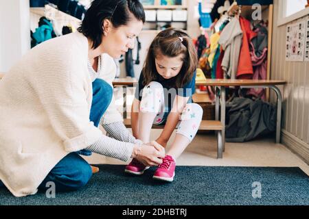 Vista laterale dell'insegnante che aiuta la ragazza a indossare scarpe nel guardaroba a prescolare Foto Stock