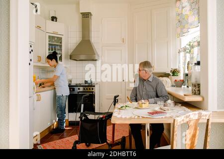 Uomo anziano in pensione che guarda la giovane donna che si occupa di assistenza cucina Foto Stock