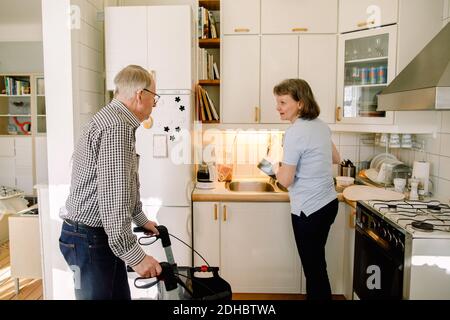 Uomo anziano pensionato che parla con i piatti volontari femminili di lavaggio dentro cucina a casa di cura Foto Stock