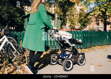 Madre che spinge la figlia in carrozza mentre cammina per recinzione dentro città Foto Stock