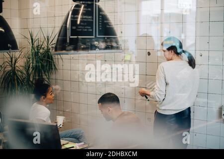 Hacker multietnici che discutono oltre il muro in ufficio creativo visto attraverso finestra Foto Stock