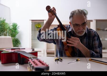 Uomo di riparazione senior che ripara gli strumenti musicali a casa Foto Stock