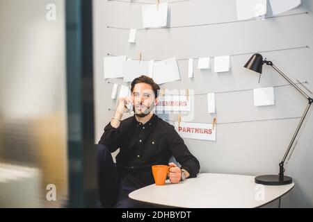 Uomo d'affari creativo che parla sul telefono cellulare mentre si è seduti alla scrivania in ufficio Foto Stock