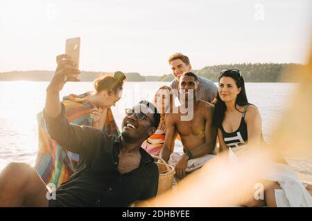 Uomo che prende selfie con amici felici con smartphone acceso molo d'estate Foto Stock