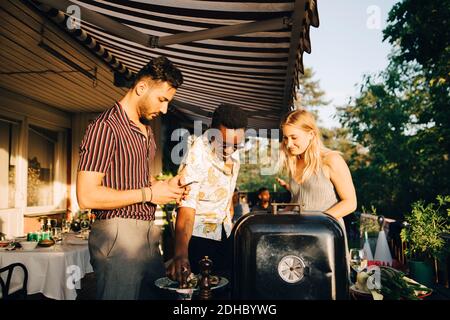 Gli amici parlano mentre gustano il cibo alla griglia durante la festa a cena cortile posteriore Foto Stock