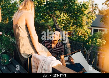 Amici che parlano alla ringhiera mentre l'uomo riposa in amaca a. iarda Foto Stock