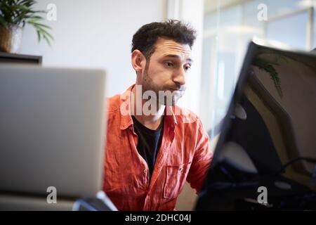 Giovane uomo d'affari creativo che fa il viso mentre lavora alla scrivania del computer in ufficio Foto Stock