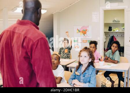 Vista posteriore degli insegnanti di sesso maschile che insegnano agli studenti in classe Foto Stock