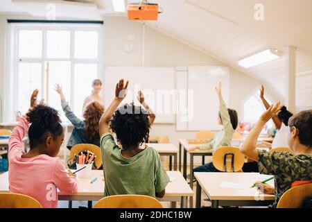 Gli studenti alzano le mani mentre rispondono in classe a scuola Foto Stock