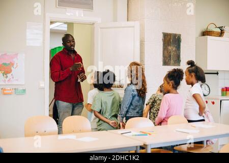 Insegnante di sesso maschile che guida e spiega gli studenti alla porta in classe Foto Stock