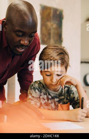 Insegnante di sesso maschile che assiste i ragazzi alla scrivania in classe Foto Stock