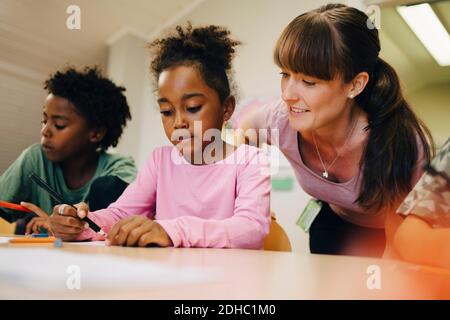 Insegnante sorridente che guarda gli studenti che disegnano in classe Foto Stock