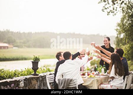 Allegri amici maschili e femminili che tostano gli occhiali durante la cena in cortile Foto Stock