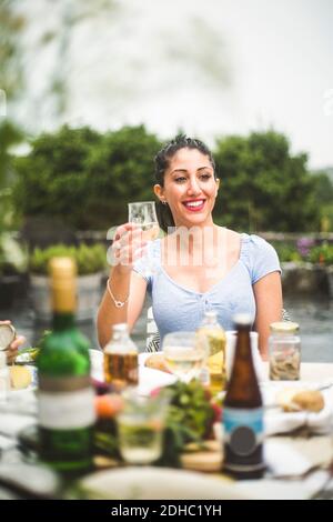 Sorridente giovane donna che guarda via mentre si gusta il vino a cena festa Foto Stock