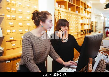 Donna matura che parla su smartphone in piedi per le vendite impiegato che usa il computer al momento del check-out nel negozio di mobili Foto Stock