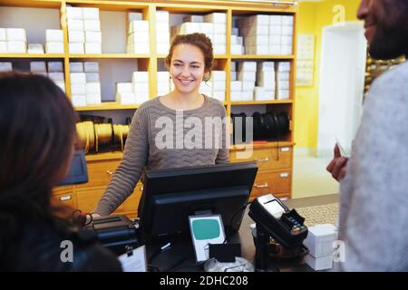 Sorridente giovane cassiera che guarda il cliente in piedi in mobili negozio Foto Stock